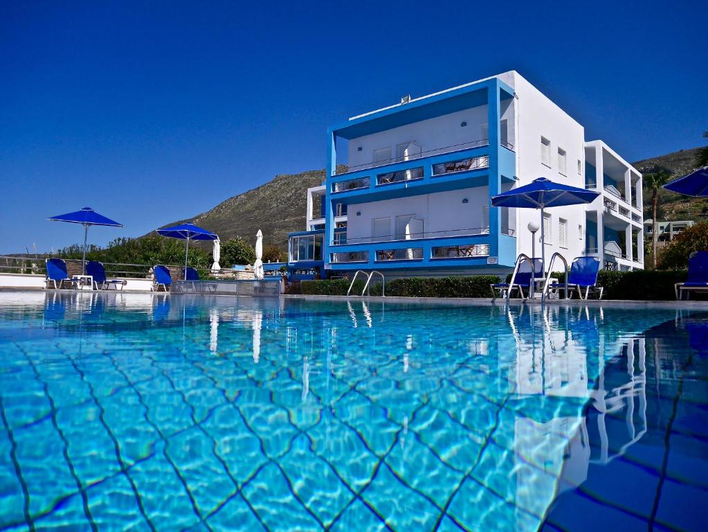 a swimming pool with chairs and umbrellas in front of a building at Kanakis Blue Beach Apartments in Petres