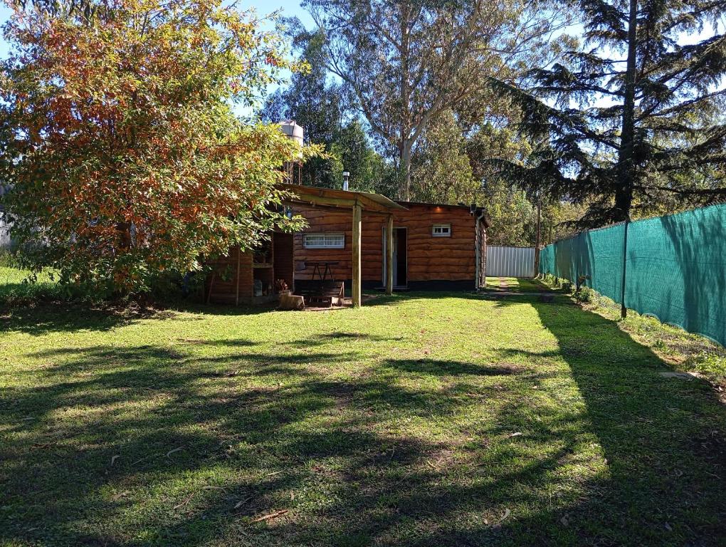 a small wooden cabin in a yard next to a fence at Cabaña Entre Arboles in Tandil