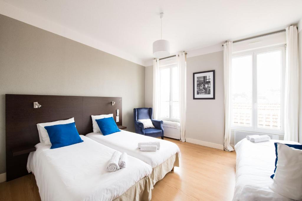 a bedroom with two beds and a blue chair at Hôtel Atrium Mondial in Lourdes