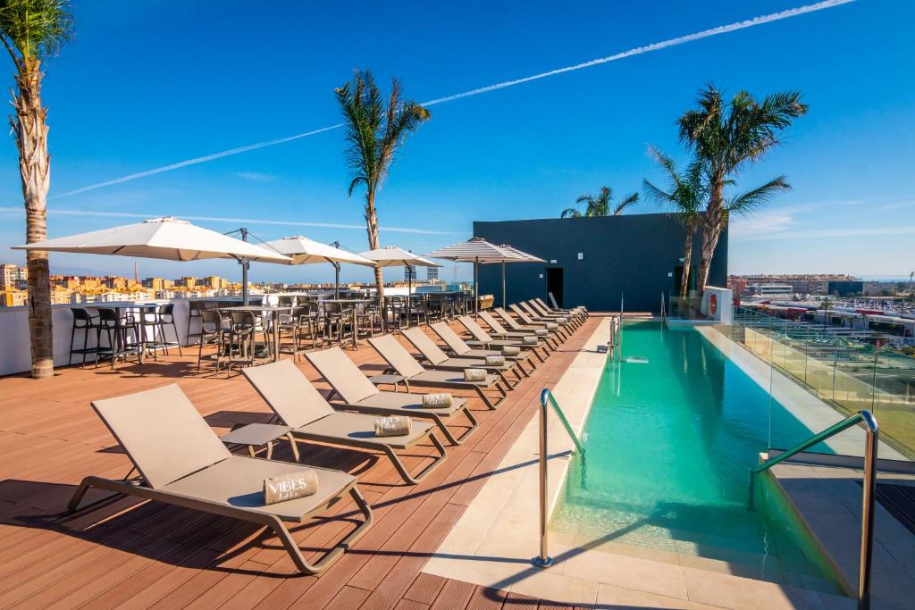a row of chairs and umbrellas next to a swimming pool at Hotel Málaga Vibes in Málaga