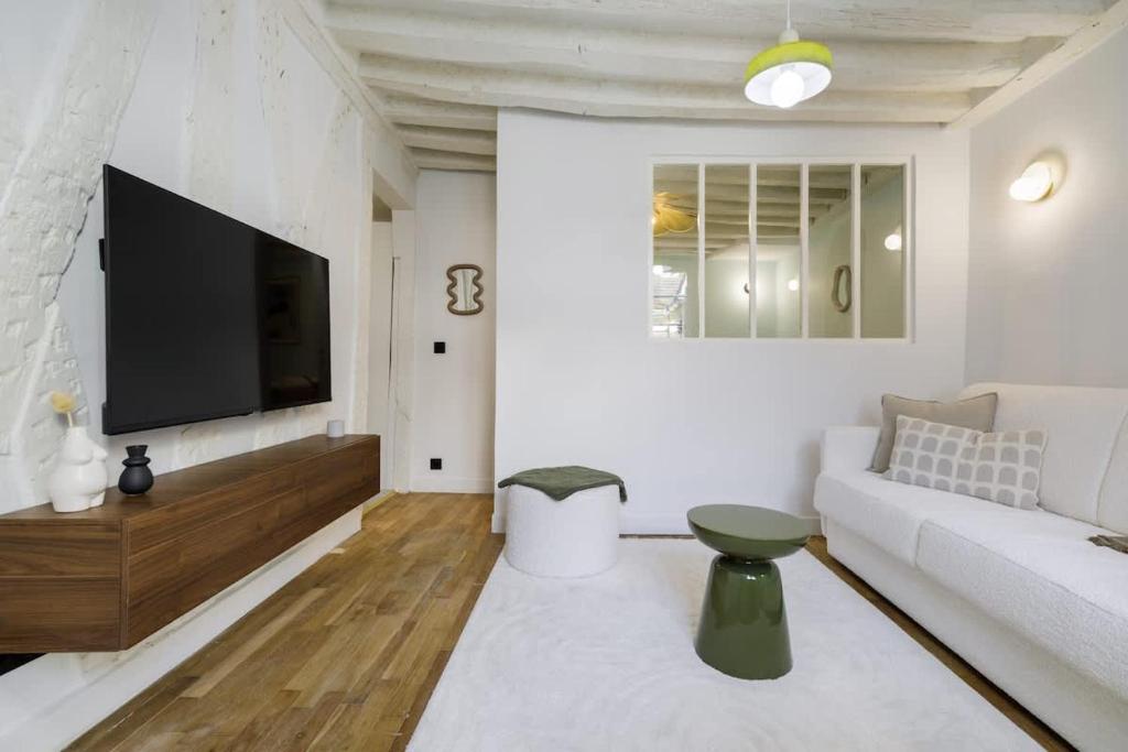 Huchette - Appartement chaleureux Paris في باريس: غرفة معيشة مع أريكة بيضاء وتلفزيون بشاشة مسطحة