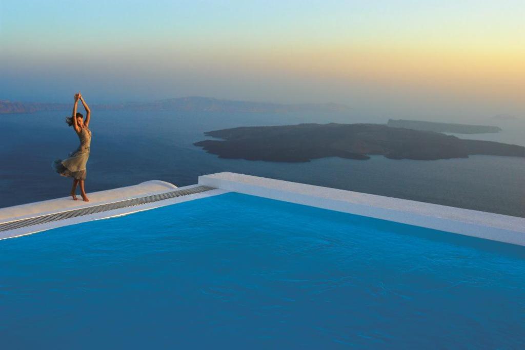 a woman standing on the edge of a swimming pool at Altana Heritage Suites in Imerovigli