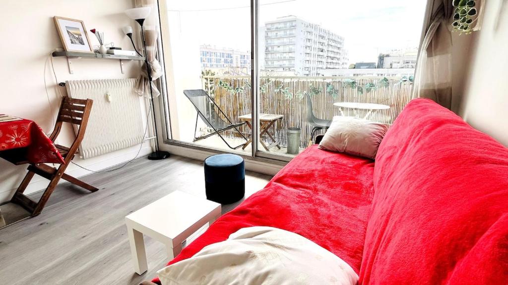 - un canapé rouge dans une chambre avec une grande fenêtre dans l'établissement Sunny Studio with Balcony - buttes Chaumont park, à Paris