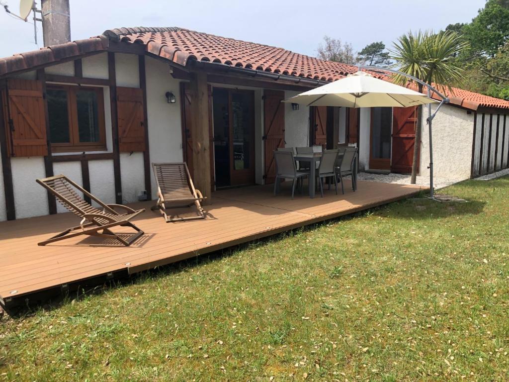 a house with a deck with chairs and an umbrella at Vieux-Boucau - Maison entière 8 pers in Soustons