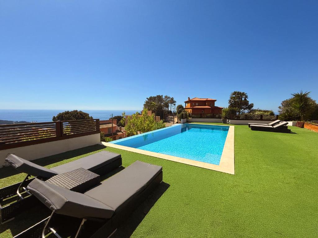 una piscina con prato verde accanto a una casa di Villa Irene - Vistas al mar a Lloret de Mar