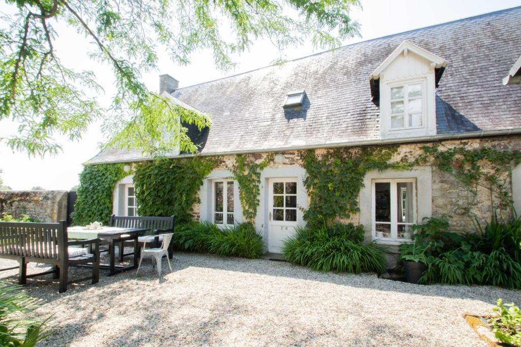 une maison avec une table et des bancs devant elle dans l'établissement Charmant cottage normand avec vue panoramique sur la côte de Regnéville, à Regnéville-sur-Mer