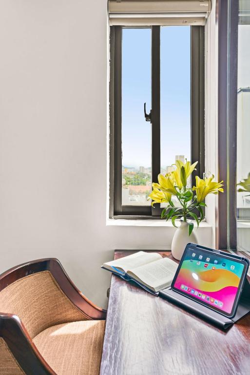 A desk beside a bright window, shown with a tablet, reading material and flowers.