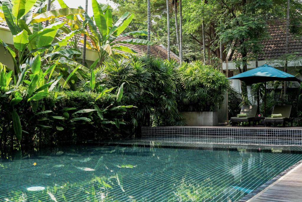 a swimming pool in a garden with a umbrella at Lynnaya Urban River Resort in Siem Reap