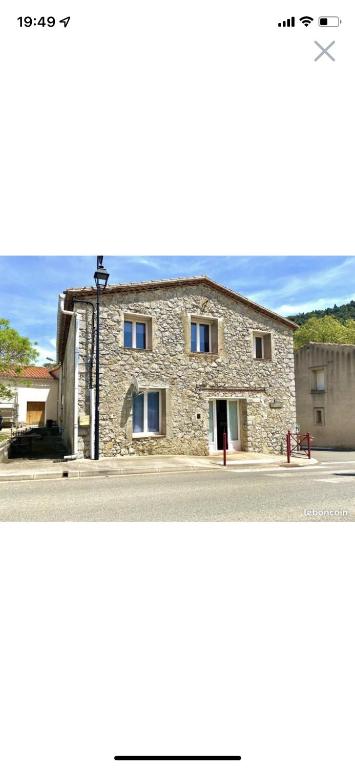 un bâtiment en pierre avec des fenêtres bleues sur une rue dans l'établissement La forge, à Laroque-de-Fa