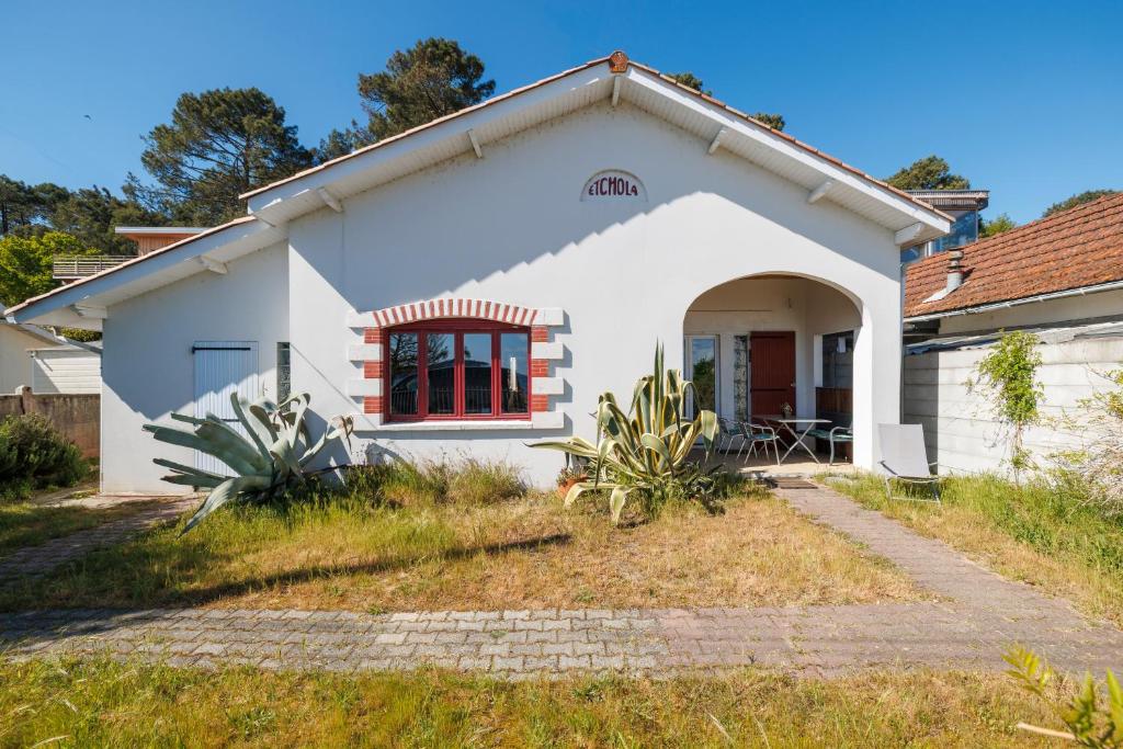 a white house with a red window in a yard at Villa Etchola - Moutchic -3 étoiles in Lacanau