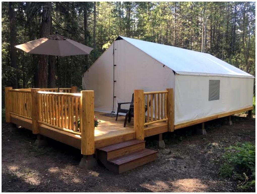 a yurt with a wooden deck and an umbrella at Gorgeous Luxury Tent Rental near Glacier National Park in Montana in Outback Mobile Home Settlement