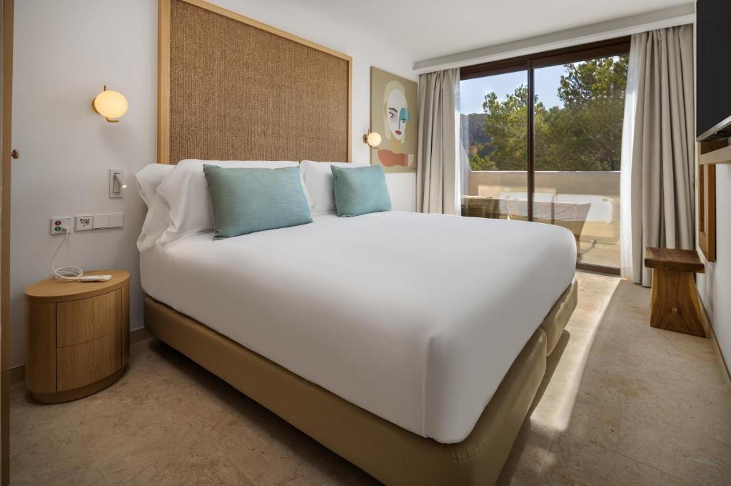a large white bed in a room with a balcony at Cala San Miguel Ibiza Resort, Adults only, Curio Collection by Hilton in Puerto de San Miguel