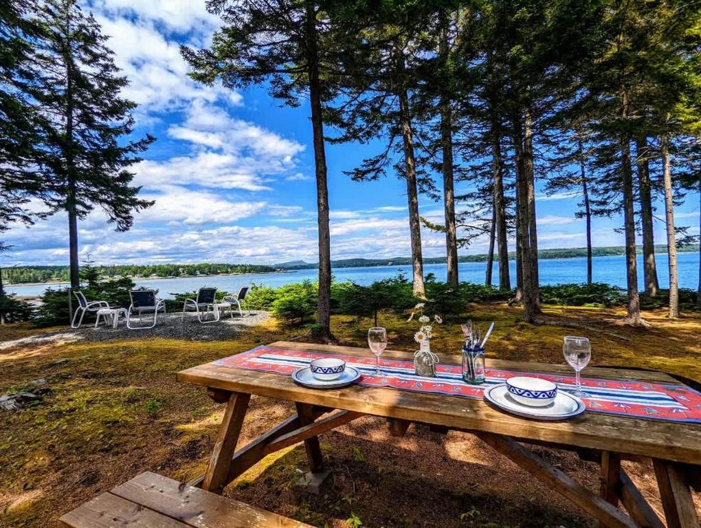 a picnic table with wine glasses and a view of the water at Couples Cove Cottage in Ellsworth