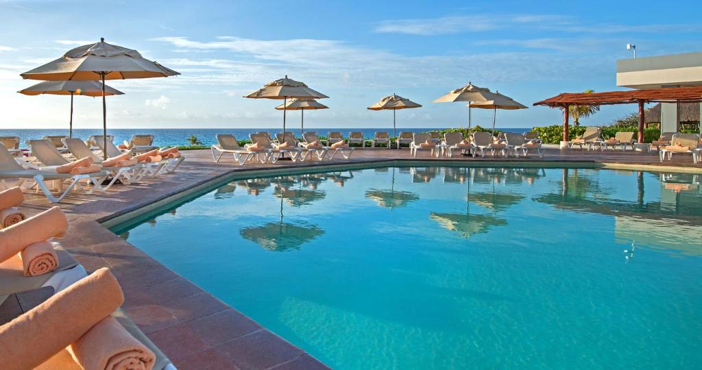 Swimming pool with loungers, umbrellas, and ocean view beyond the deck.