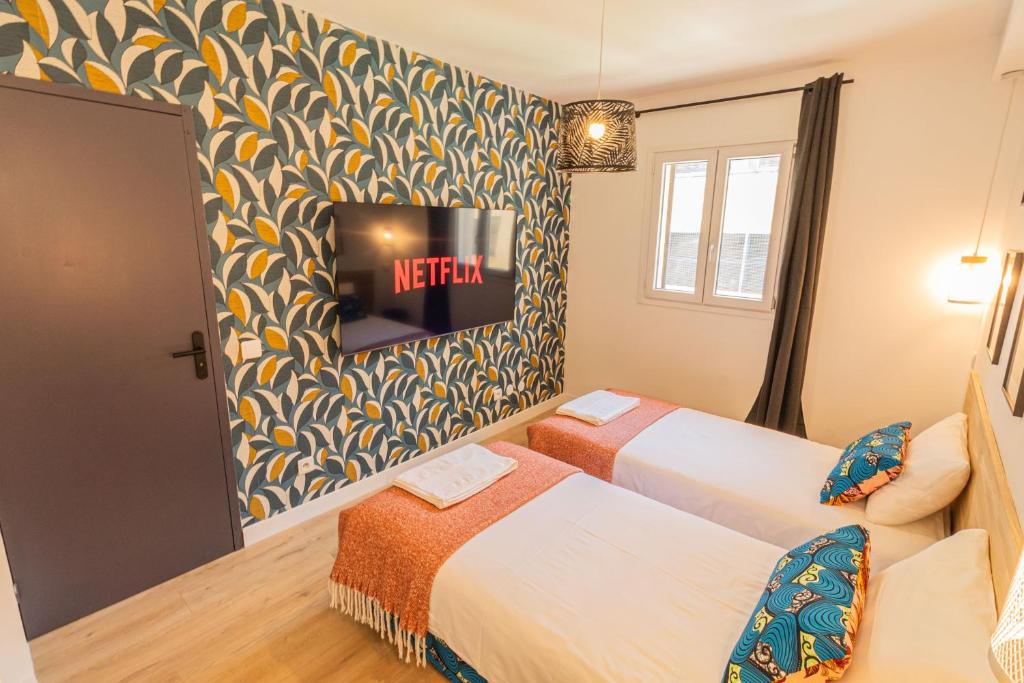 a hotel room with two beds and a tv on the wall at AfroBoHome, Expérience Atypique, clim, 2 à 6 personnes, Proche centre Nîmes, Garage clos in Nîmes