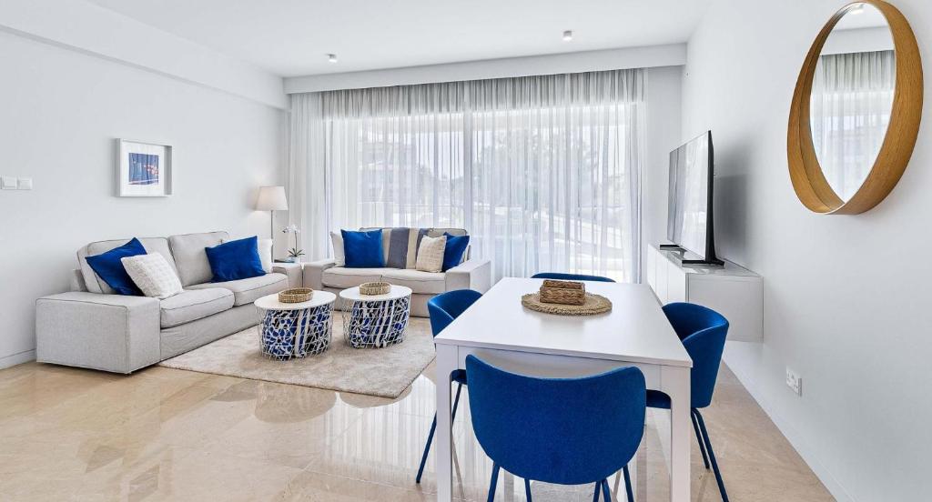 sala de estar con mesa blanca y sillas azules en Brand New Stunning Apartment with Pool Views, Dionysus Village, Aphrodite Hills, en Kouklia