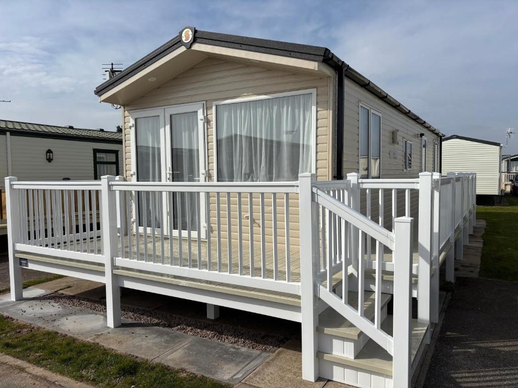 a small house with a white railing and a porch at Palm Grove 19 - Golden Palm - Central Heating, WiFi, pet friendly, bed linen - Meadow Lakes Caravan & Lodge Hire in Chapel Saint Leonards