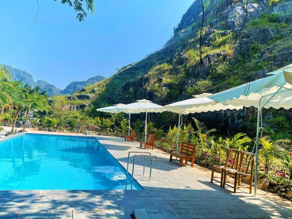 a swimming pool with chairs and umbrellas next to a mountain at TRang an Mountain Ecolodge in Xuân Sơn