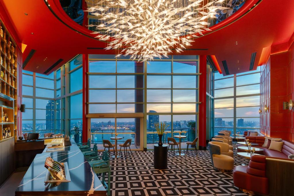 A dramatic, window-lined lounge has a chandelier, patterned flooring, and river-facing seating.