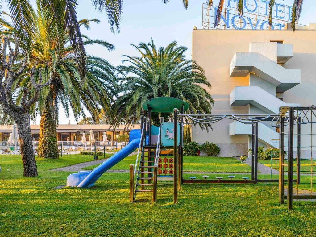 a playground with a slide in a park with palm trees at Novotel Porto Gaia in Vila Nova de Gaia