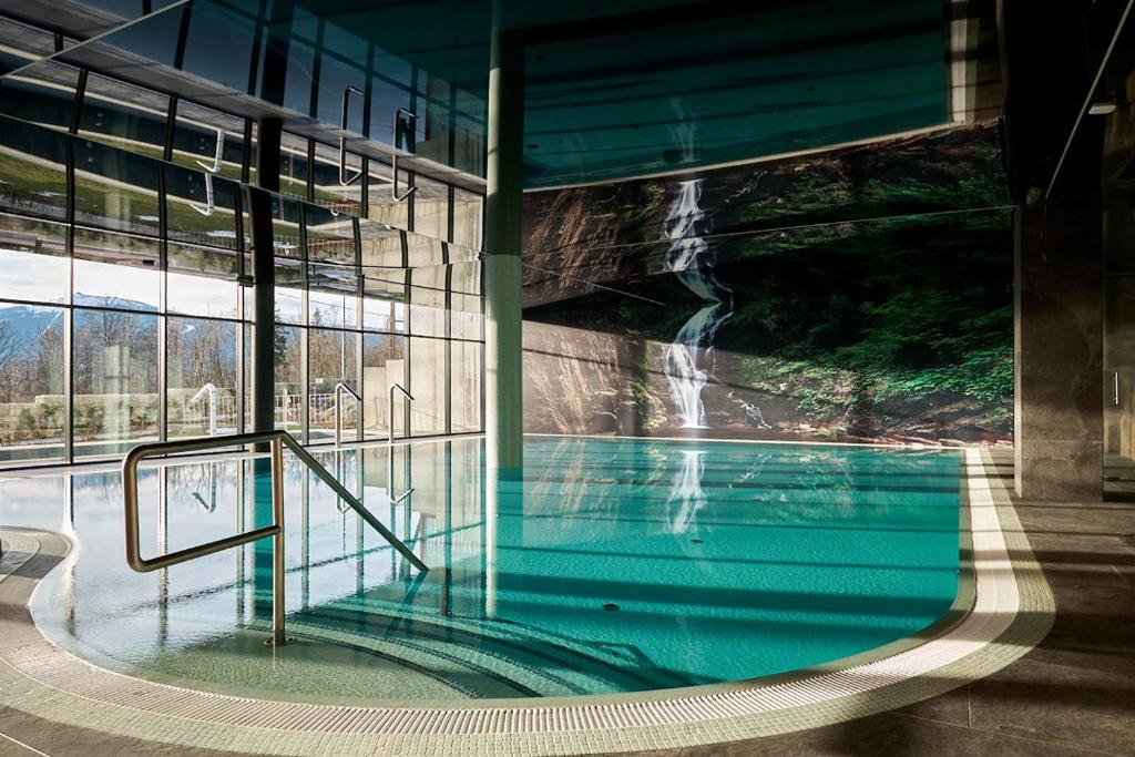 Curved indoor pool with handrail, steps and large waterfall mural reflected in water.