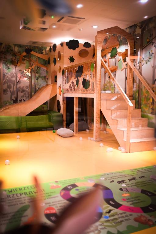 Indoor children's playroom featuring a wooden climbing structure with slide and scattered white play balls on floor