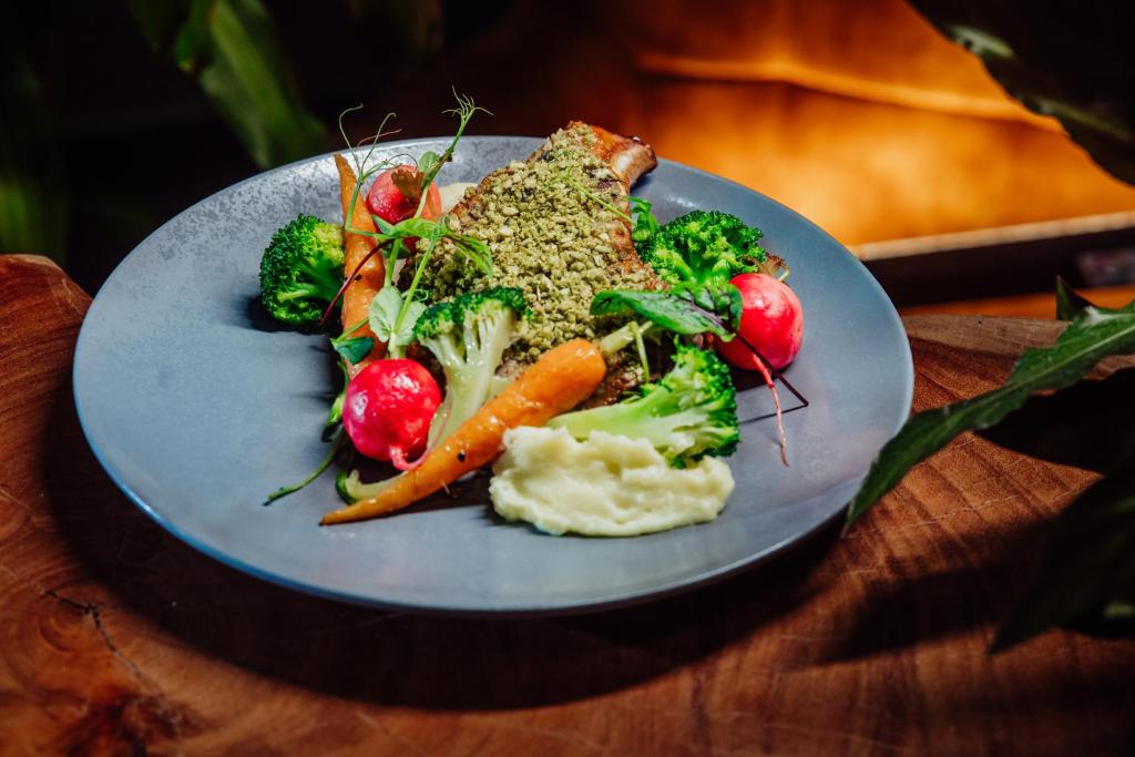 Herb-crusted meat with mashed potato, steamed broccoli, radishes and baby carrot on a gray plate