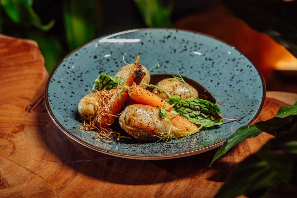 Blue speckled bowl with roasted potatoes, glazed baby carrots, crispy garnish and fresh greens, rustic presentation