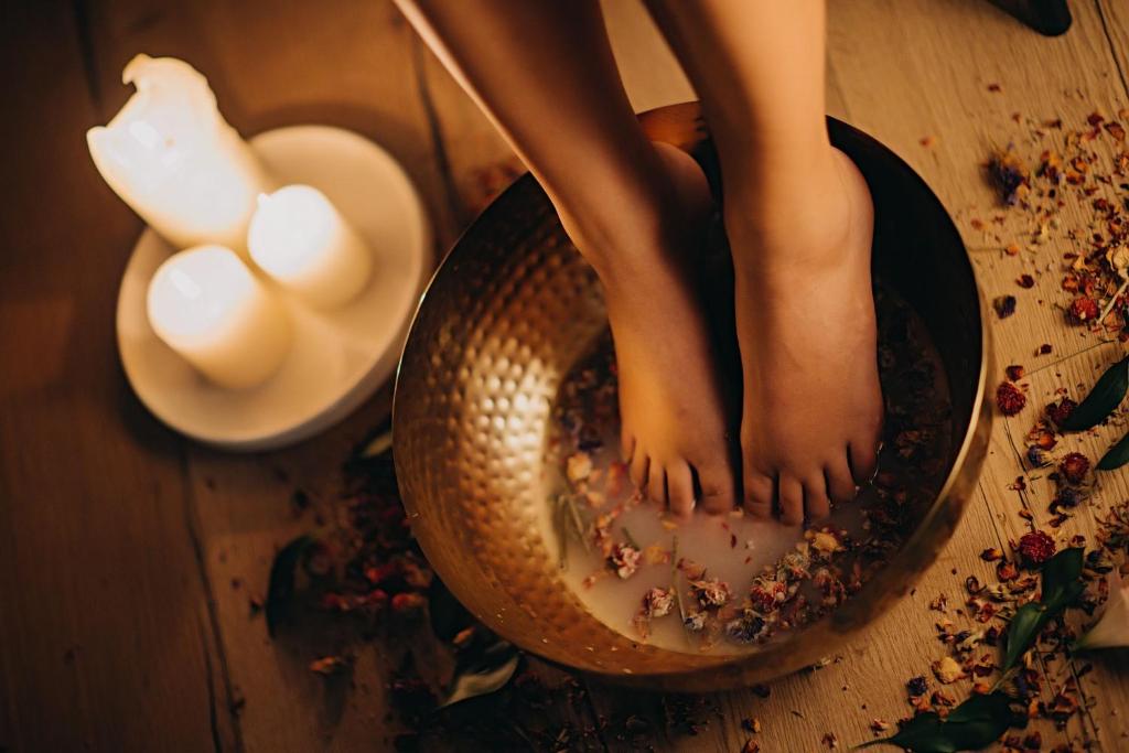 Feet soaking in a floral milk foot bath beside lit candles, warm relaxing spa mood