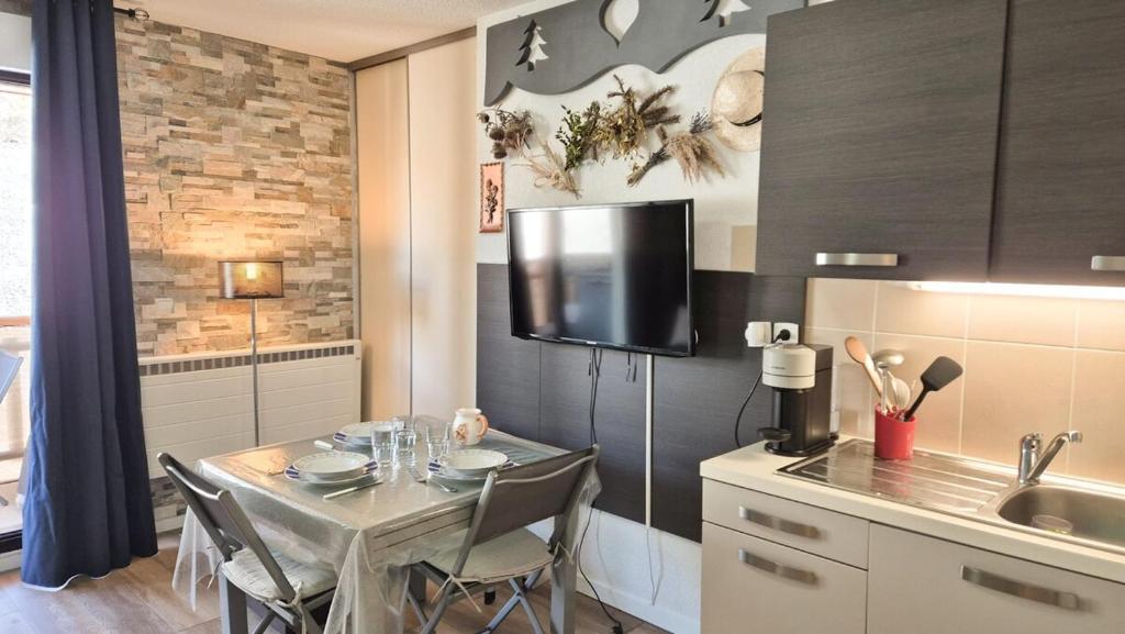 Il comprend une cuisine avec une table et une télévision murale. dans l'établissement Studio cosy au cœur de la station avec piscine, à Péone