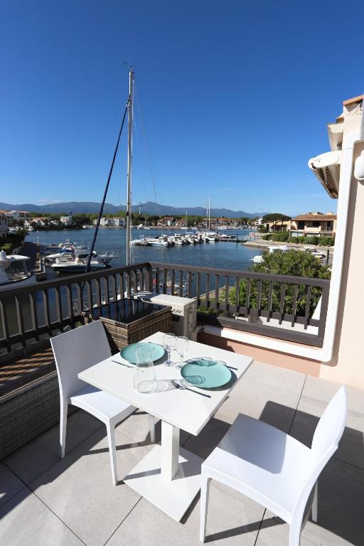 - une table et des chaises blanches sur un balcon avec un port dans l'établissement Spacieux Studio 3pers vue marina a St Cyprien, à Saint-Cyprien