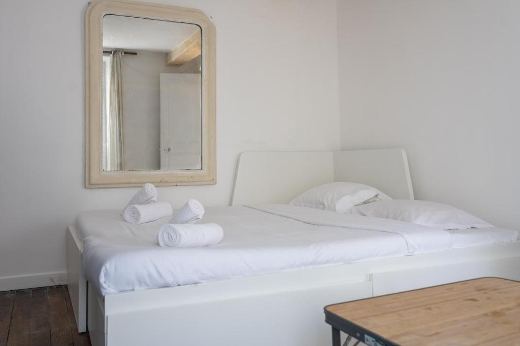 a white bed with towels on it with a mirror at Bright and Cosy studio apartment in Republique Paris in Paris