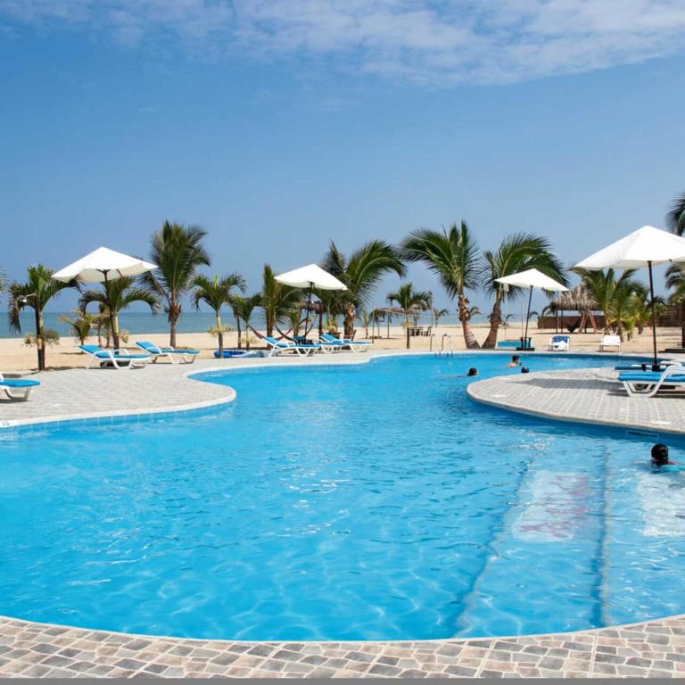 a large pool with chairs and umbrellas on a beach at Nauti-k Beach Hotel in Tumbes