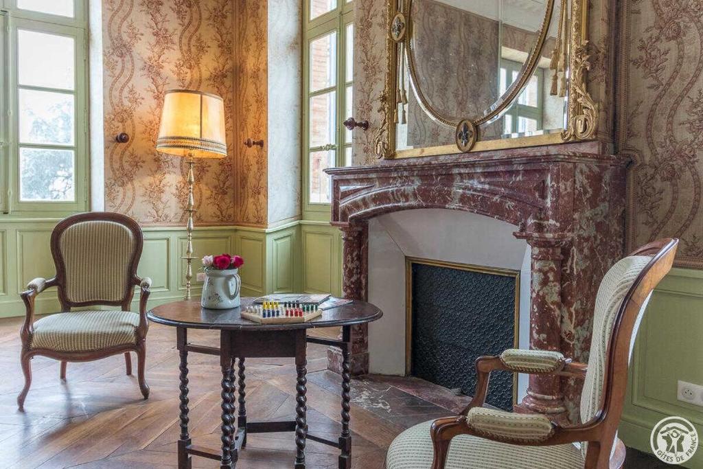 a living room with a fireplace and a table and chairs at Château de puydaniel in Puydaniel