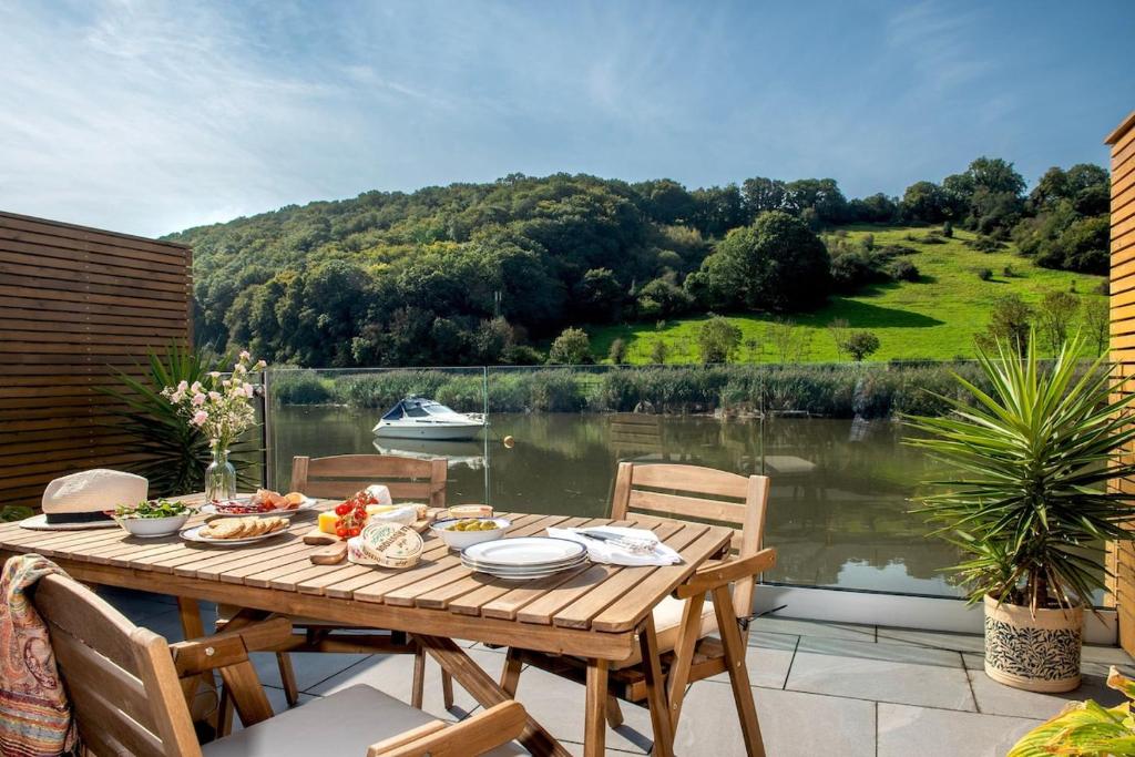 einen Holztisch auf einer Terrasse mit Seeblick in der Unterkunft Waterfront Cottage - Apple Pie Luxury Escapes in Calstock