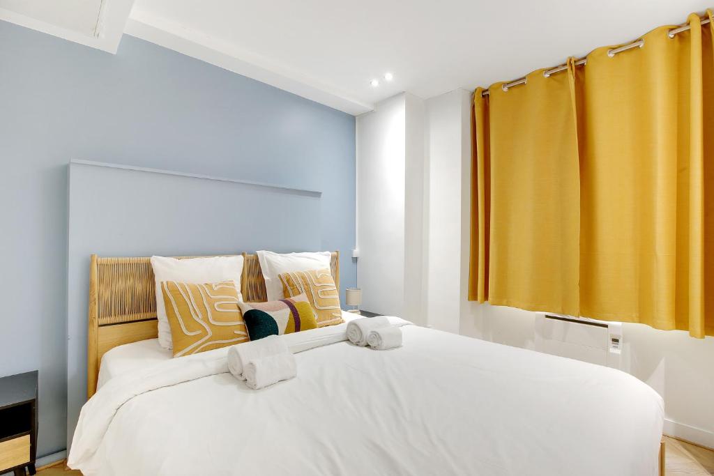 - une chambre avec un grand lit blanc et des rideaux jaunes dans l'établissement Charmant cocon design 1BR - Proche Montmatre, à Paris