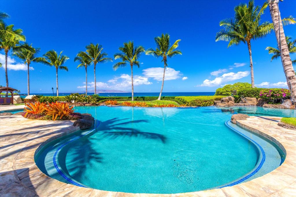 a swimming pool with palm trees and the ocean at Ocean View Luxury, Castaway Cove C201, Wailea Beach Villas! in Wailea