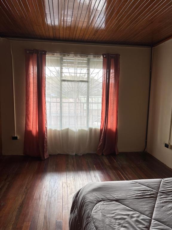 a bedroom with a bed and a window with red curtains at El Garaje b&b in Zarcero