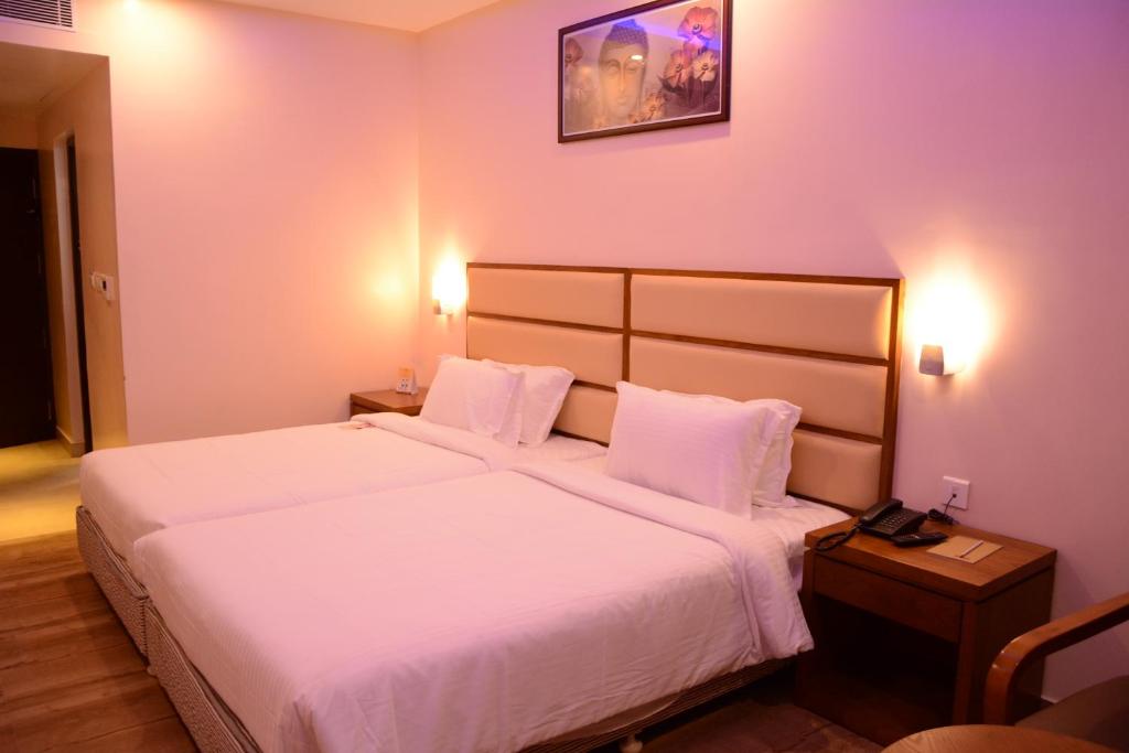 una habitación de hotel con una cama grande con sábanas blancas en Kani Residency Hotel, en Thoothukudi