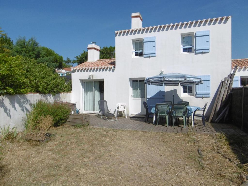 une maison blanche avec une terrasse dotée de chaises et d'un parasol dans l'établissement Maison confortable à Barbâtre pour 4 personnes, proche plage - FR-1-823-150, à Barbâtre