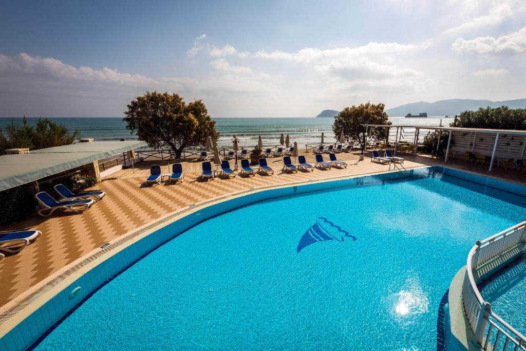 
a beach with a pool and chairs and a blue sky at Mediterranean Beach Resort in Laganas

