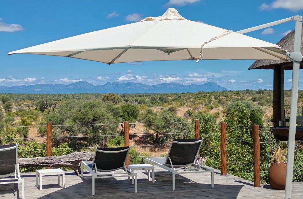 a patio with chairs and an umbrella and mountains at Sausage Tree Safari Camp in Balule Game Reserve