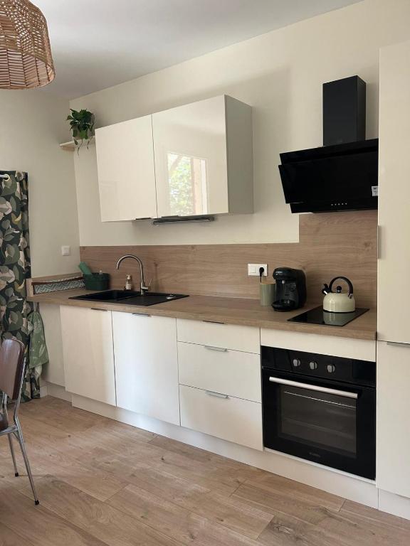 une cuisine avec des armoires blanches, un évier et une cuisinière dans l'établissement cozy and central, à Millau