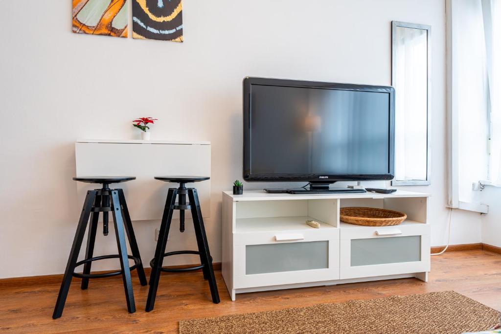- une télévision installée au-dessus d'un centre de divertissement blanc avec deux tabourets dans l'établissement ApartStudio 224 - Zagreb - WIFI, à Zagreb