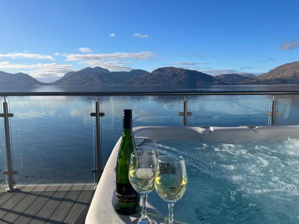 two bottles and glasses of wine sitting next to a swimming pool at Loch Linnhe Waterfront Lodges with Hot Tubs in Glencoe
