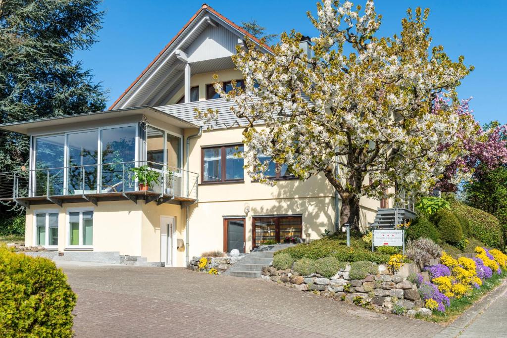 a white house with a tree and flowers at Haus Annette in Immenstaad am Bodensee