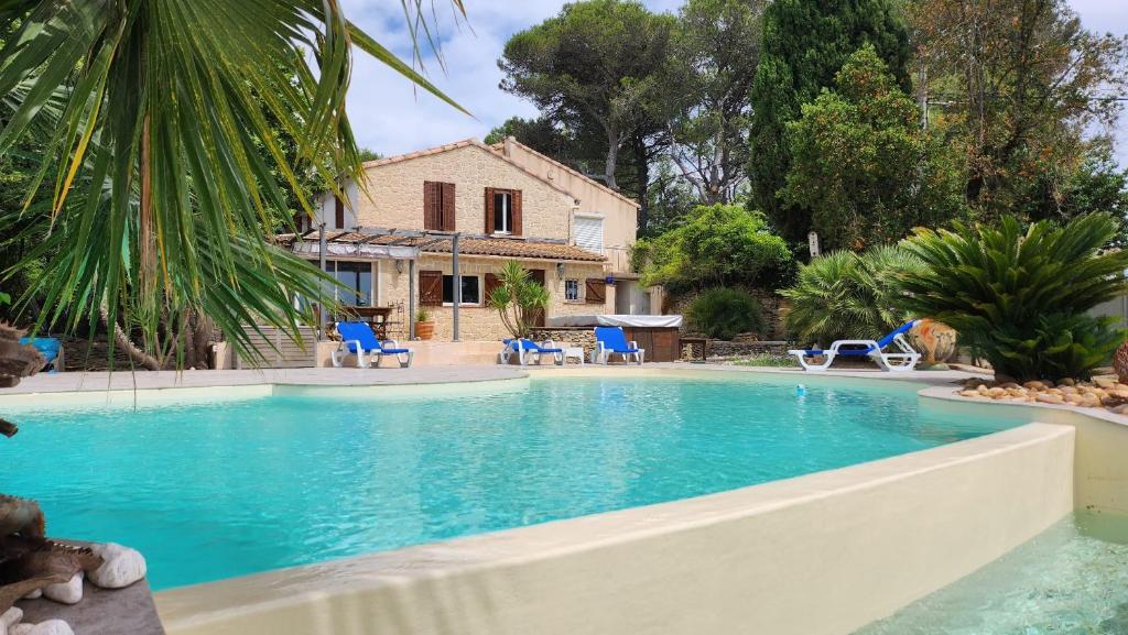 une piscine avec des chaises bleues et une maison dans l'établissement Villa de standing avec piscine à débordement, jacuzzi et jardin à 5 min du centre de Nîmes, à Nîmes
