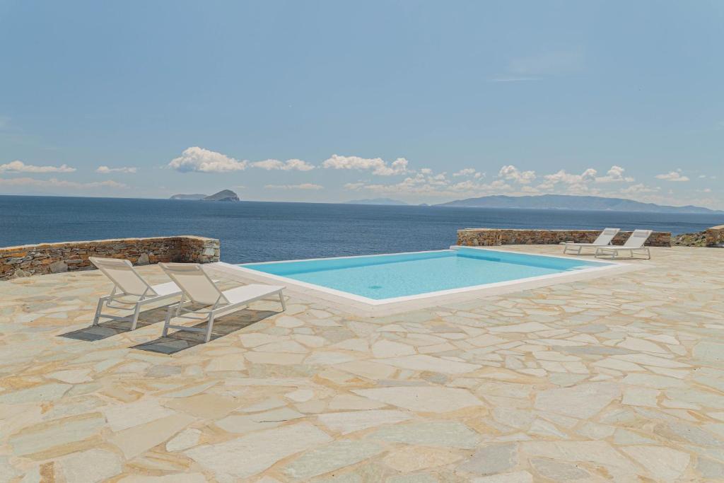 a swimming pool with two chairs and the ocean at Infinity Blue Villas, Kythnos in Kithnos