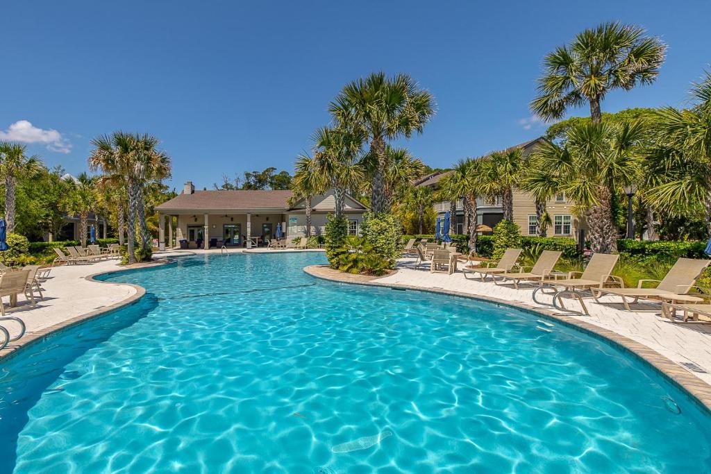 a swimming pool with chairs and palm trees at Garden Cottage 62 in Jekyll Island