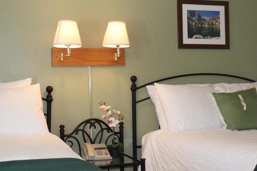 two beds in a room with two lamps and a table at Trees Motel in Bishop